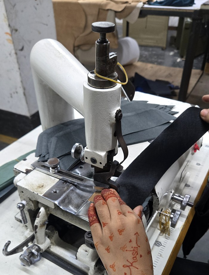 A worker's hand, marked with henna, guiding leather through a skiving machine