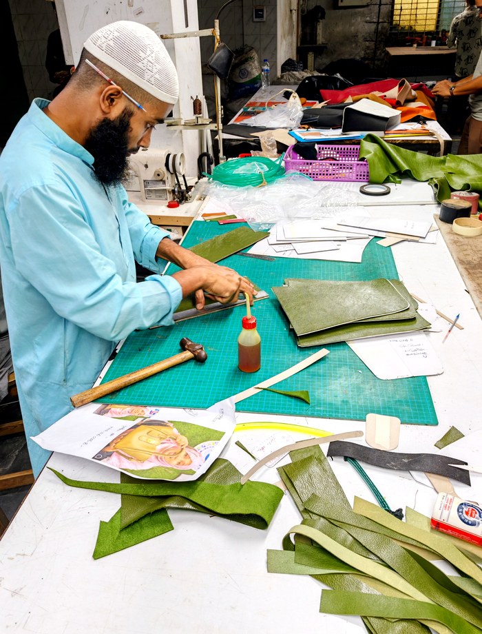 A craftsman carefully working leather at his bench, tools and offcuts around him