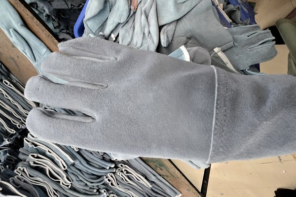 Split leather work gloves held up with bulk production in background